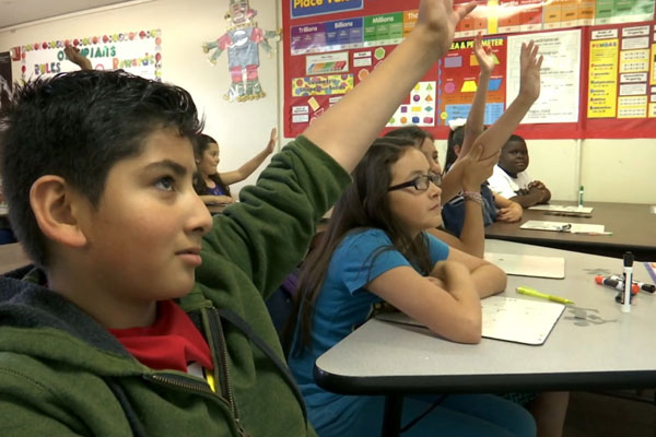 Students raising thier hands to answer questions in the classroom.